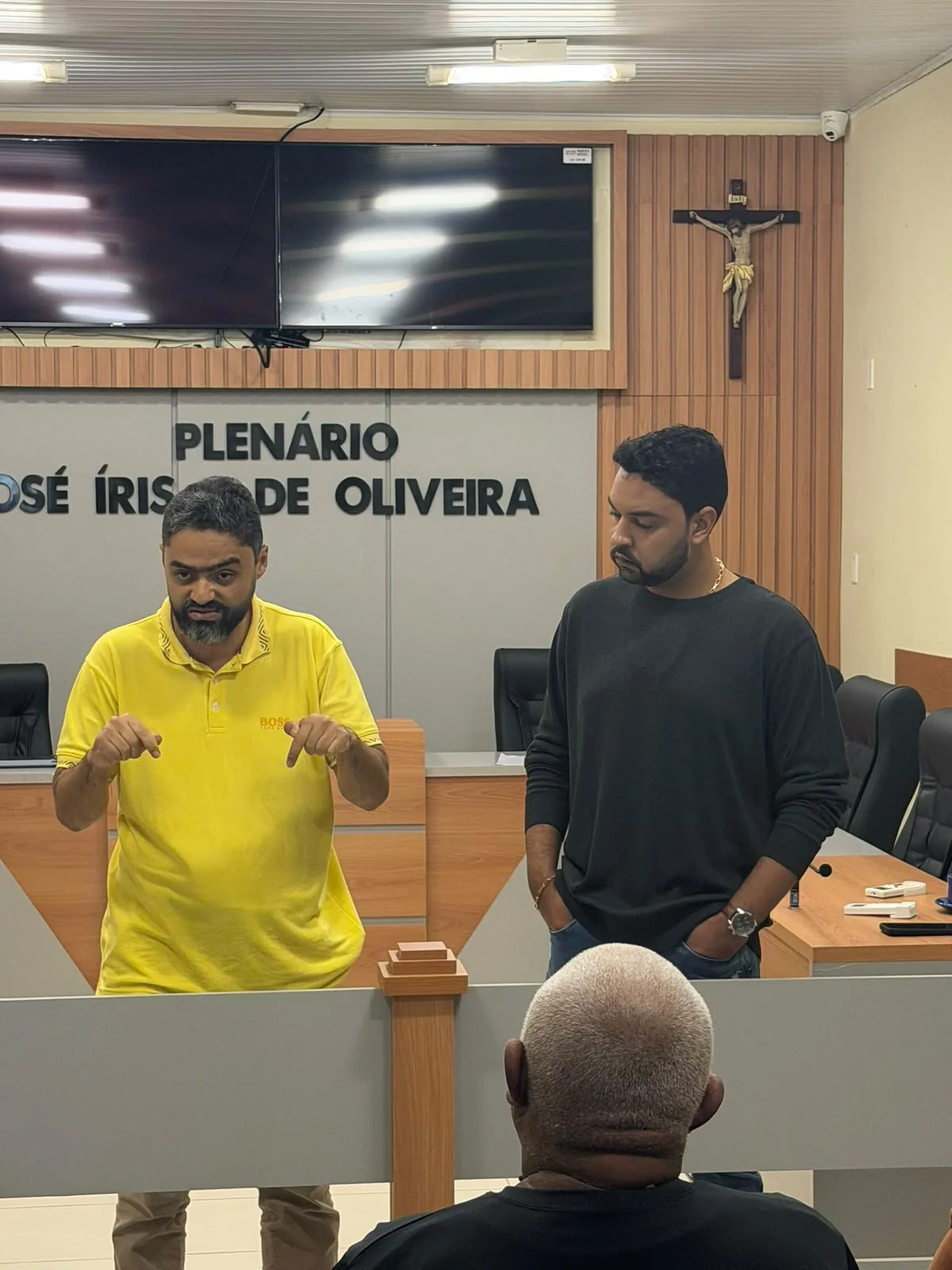 Dois participantes em pé conversando diante de público em plenário